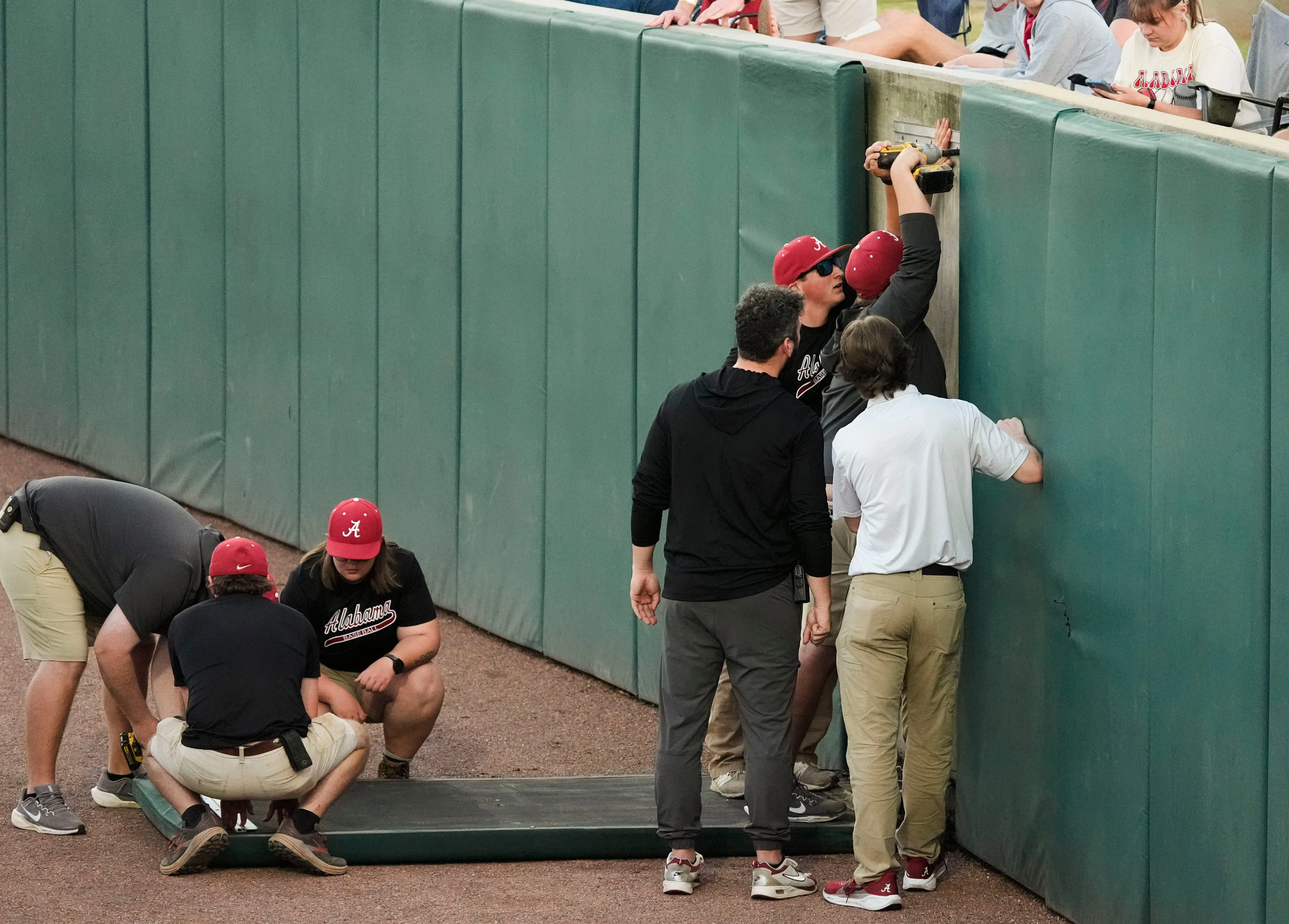 Members of the ground crew works to fix a fallen pad along the right field fence at Sewell-Thomas Stadium for the SEC home opener against Florida.