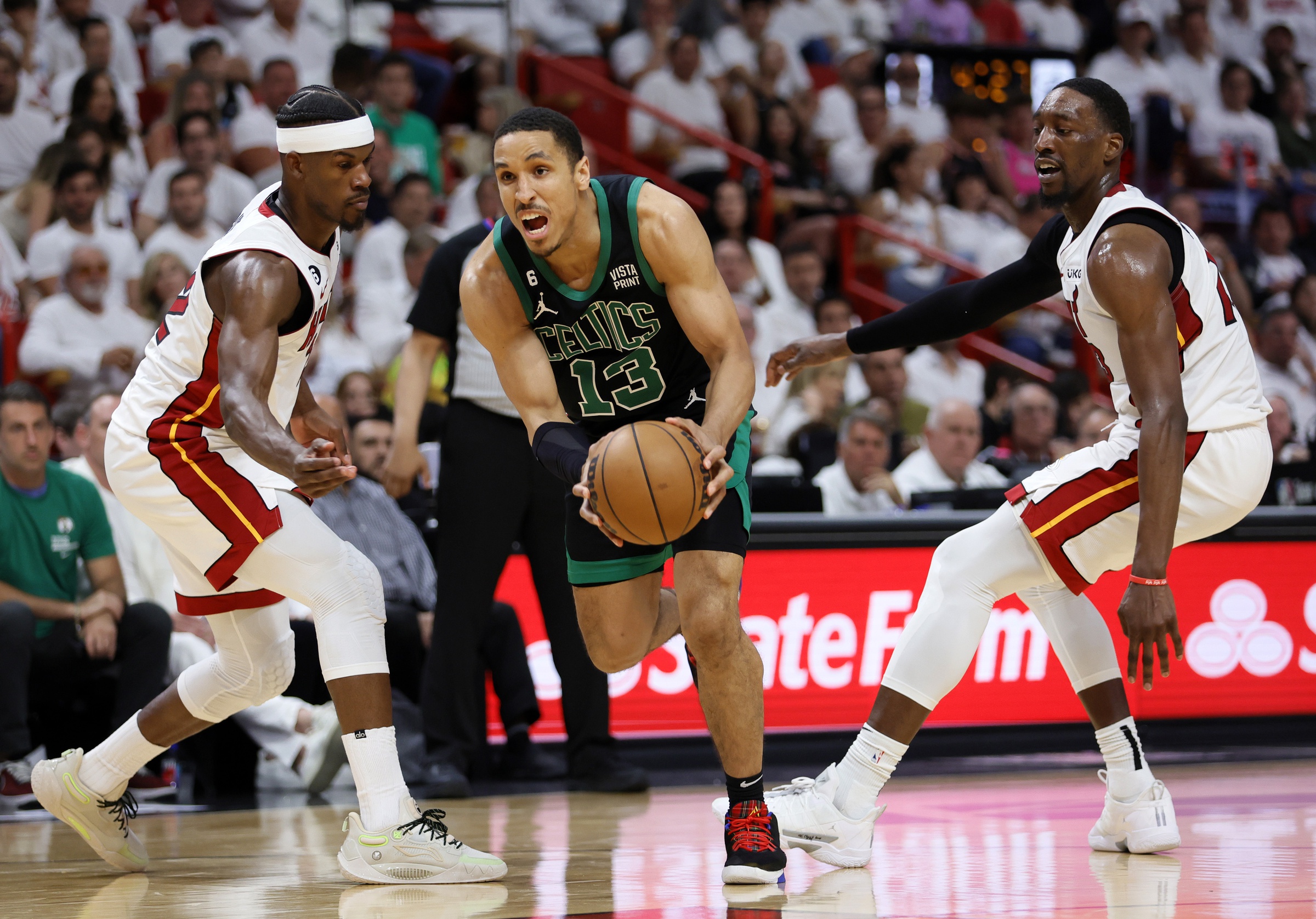 May 21, 2023; Miami, Florida, USA; Boston Celtics guard Malcolm Brogdon (13) drives against Miami Heat forward Jimmy Butler (22) and center Bam Adebayo (13) during the third quarter in game three of the Eastern Conference Finals for the 2023 NBA playoffs at Kaseya Center. Mandatory Credit: Sam Navarro-USA TODAY Sports