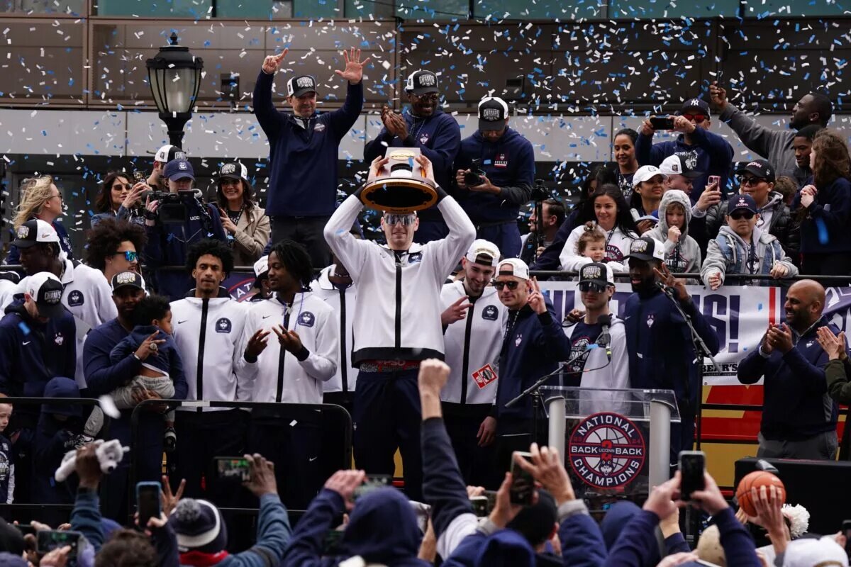 UConn Huskies center Donovan Clingan (32) hold up the championship trophy as the team celebrates in front of a large crowd of fans after the teams victory parade.