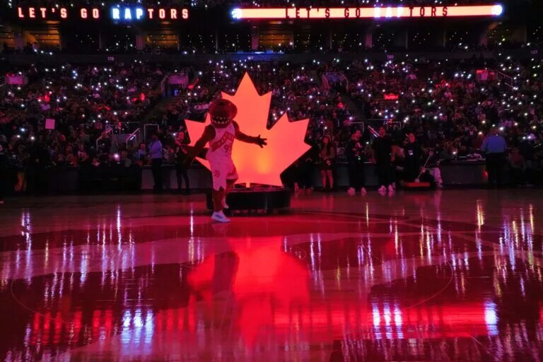 The Toronto Raptors mascot poses in front of a maple logo at center court