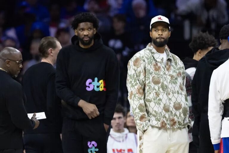 Injured Philadelphia 76ers Paul George (R) and Joel Embiid (L) look on during the first quarter