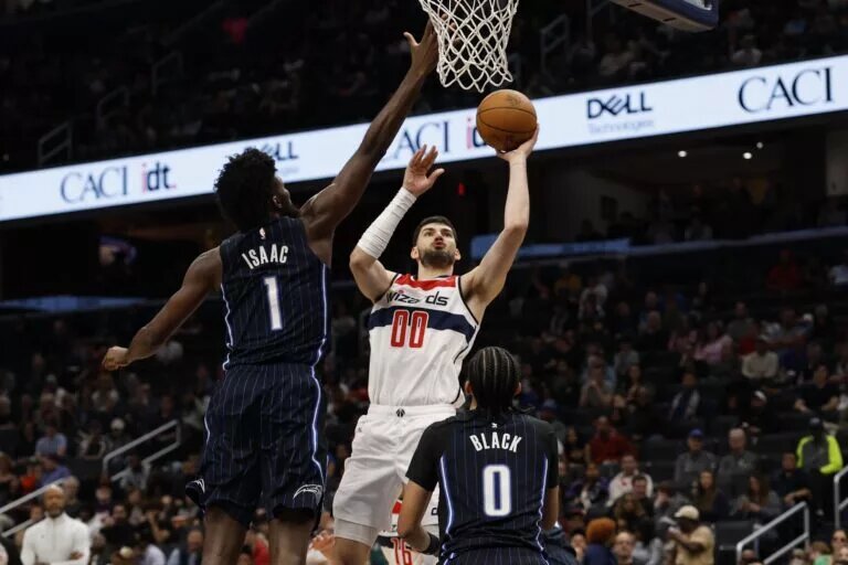 Apr 3, 2025; Washington, District of Columbia, USA; Washington Wizards forward Tristan Vukcevic (00) shoots the ball as Orlando Magic forward Jonathan Isaac (1) defends in the second half at Capital One Arena. Mandatory Credit: Geoff Burke-Imagn Images