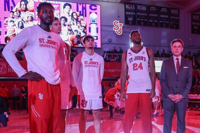 Nov 3, 2025; Queens, New York, USA; St. John's Red Storm forwards Sadiku Ibine Ayo (2), Rubén Prey (17), guard Lefteris Liotopoulos (31) and forward Zuby Ejiofor (24) stand with head coach Rick Pitino prior to the raising of the 2025 Big East Championship banner at Carnesecca Arena. Mandatory Credit: Wendell Cruz-Imagn Images