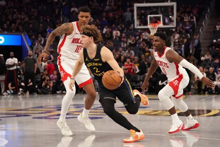 Nov 26, 2025; San Francisco, California, USA; Golden State Warriors guard Brandin Podziemski (2) drives between Houston Rockets forward Jabari Smith (10) and guard Aaron Holiday (0) in the fourth quarter at Chase Center. Mandatory Credit: David Gonzales-Imagn Images