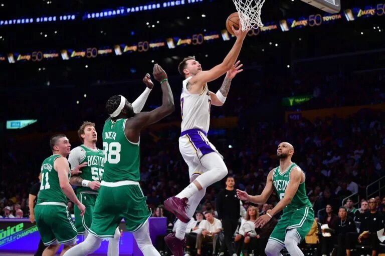 Feb 22, 2026; Los Angeles, California, USA; Los Angeles Lakers guard Luka Doncic (77) moves to the basket agianst Boston Celtics center Neemias Queta (88) and guard Derrick White (9) during the second half at Crypto.com Arena. Mandatory Credit: Gary A. Vasquez-Imagn Images