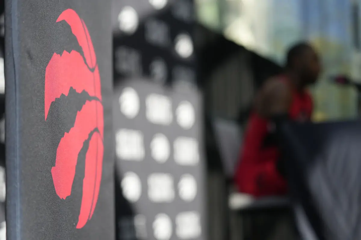 Toronto Raptors logo on display during media day press conference with obscure player in background