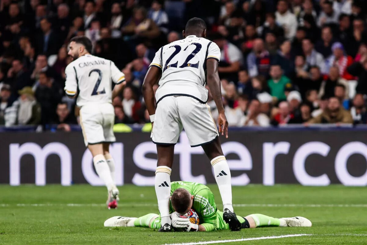 Real Madrid's Andriy Lunin holds ball while Antonio Rudiger shields him.