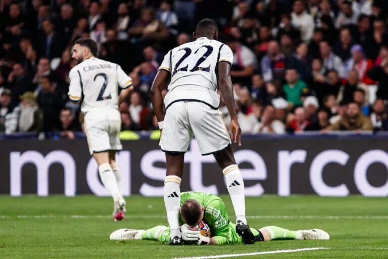 Real Madrid's Andriy Lunin holds ball while Antonio Rudiger shields him.