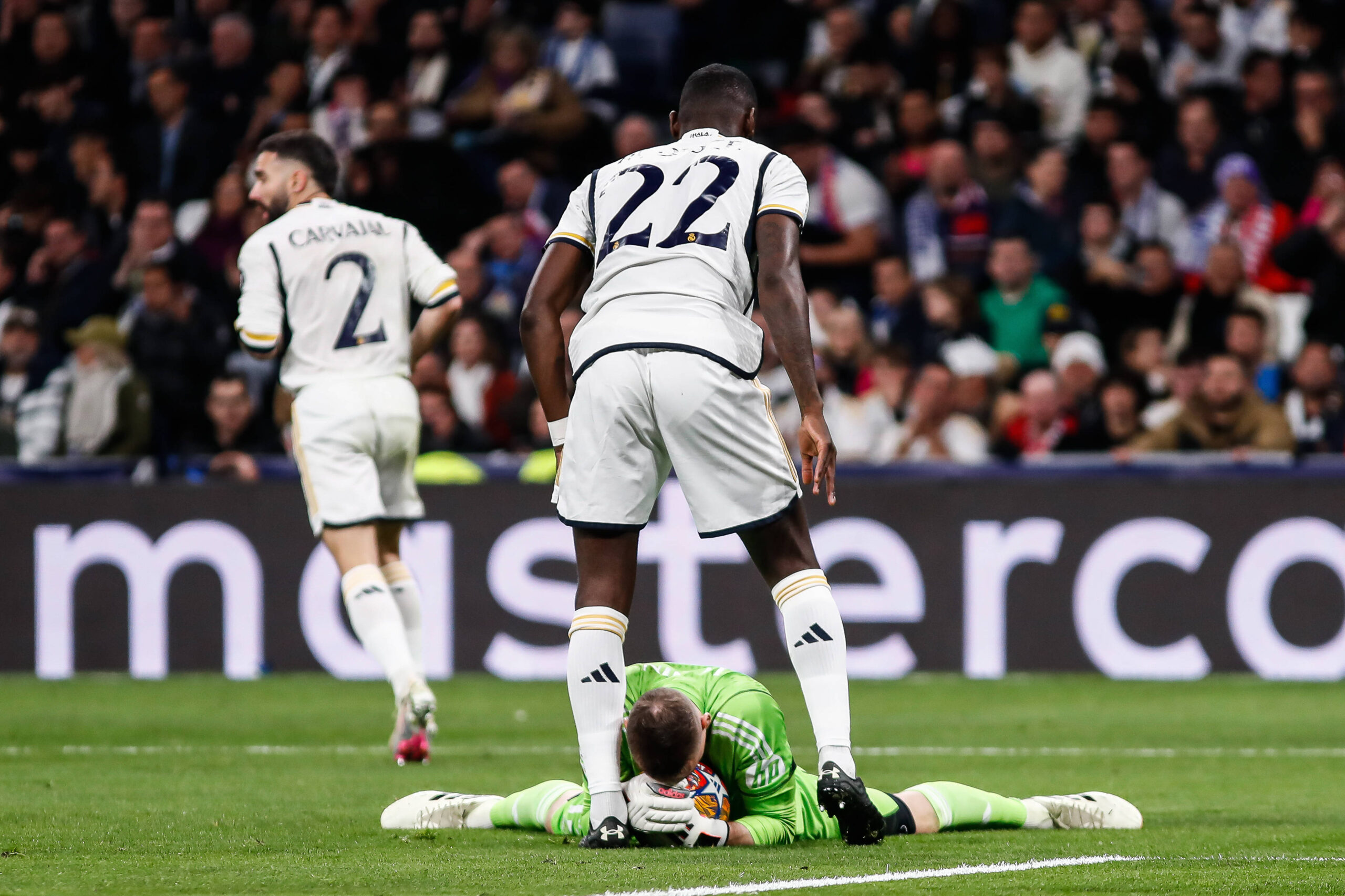 Real Madrid's Andriy Lunin holds ball while Antonio Rudiger shields him.