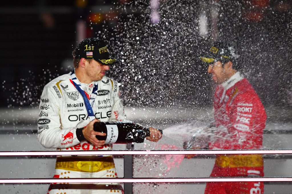 Max Verstappen and Sergio Perez spraying champagne on the podium of the Las Vegas Grand Prix, 2023