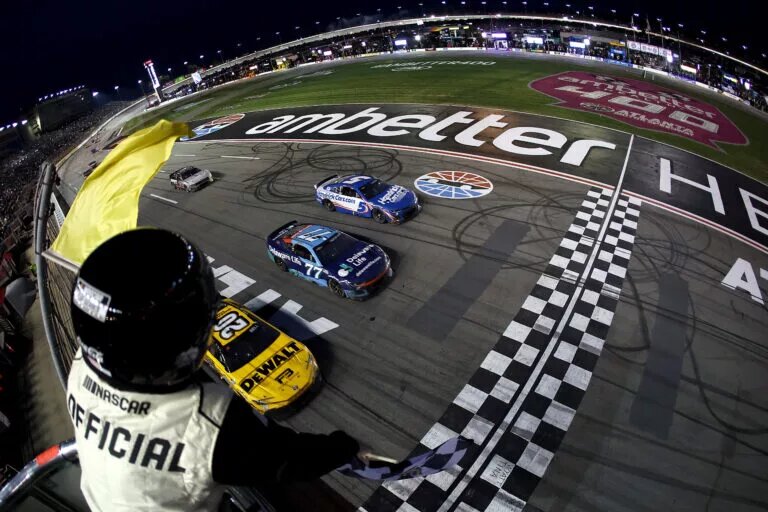 HAMPTON, GEORGIA - FEBRUARY 23: Christopher Bell, driver of the #20 DEWALT Toyota, takes the checkered flag under caution to win ahead of Carson Hocevar, driver of the #77 Delaware Life Chevrolet, and Kyle Larson, driver of the #5 HendirickCars.com Chevrolet, in the NASCAR Cup Series Ambetter Health 400 at Atlanta Motor Speedway on February 23, 2025 in Hampton, Georgia. (Photo by Chris Graythen/Getty Images)
