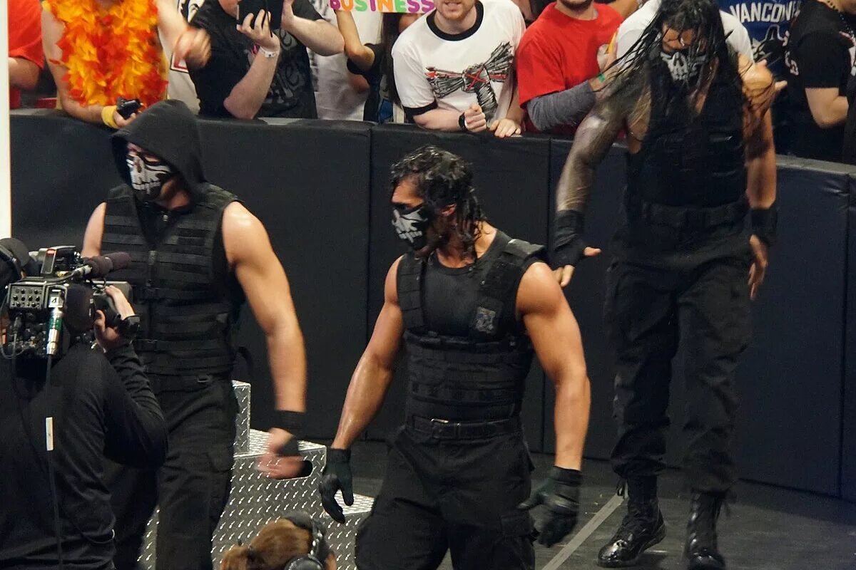 The three members of the Shield: Roman Reigns, Dean Ambrose, and Seth Rollins, make a masked entrance into the arena.