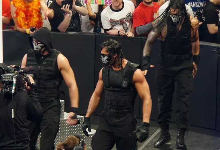 The three members of the Shield: Roman Reigns, Dean Ambrose, and Seth Rollins, make a masked entrance into the arena.